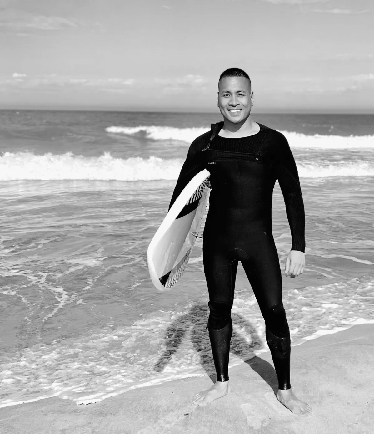 Nick Arndt, founder of White Belt Surfer, standing at the water's edge in a wetsuit holding his surfboard